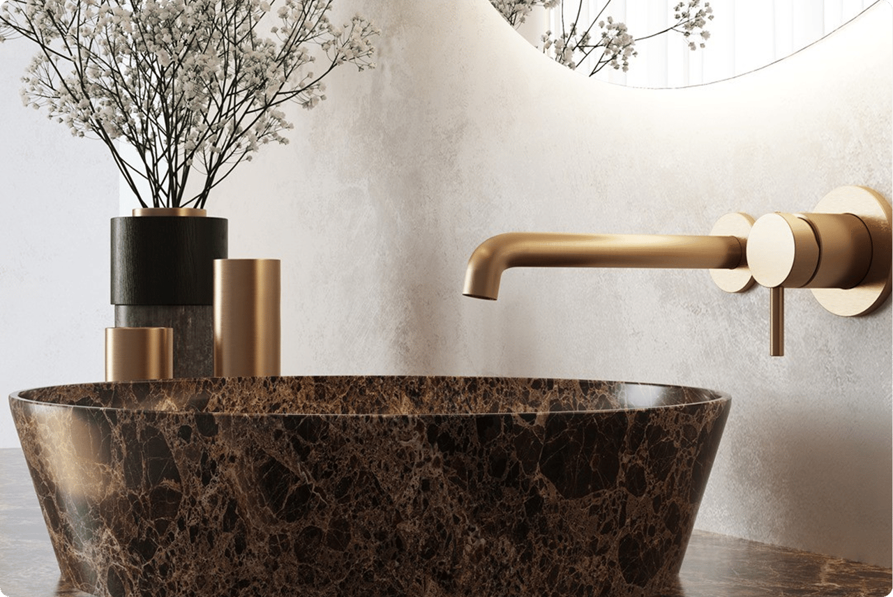 Detailansicht eines luxuriösen x²o Waschplatzes mit dunkel marmorierter Waschschale und goldfarbener Wandarmatur. Links dekorative Zylinder in Gold und Schwarz sowie feine weiße Blumen im Hintergrund. Alles ist in sanften, natürlichen Tönen gestaltet.